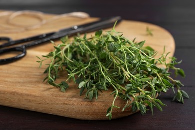 Photo of Bunch of aromatic thyme and scissors on wooden table, closeup