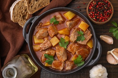 Photo of Delicious goulash in pot, bread and ingredients on wooden table, flat lay
