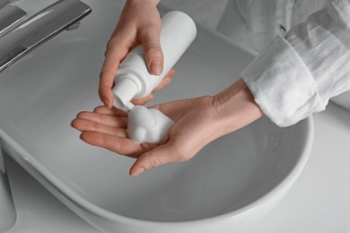 Woman washing hands with cleansing foam near sink in bathroom, closeup