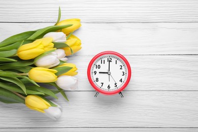 Red alarm clock and beautiful tulips on white wooden table, flat lay with space for text. Spring time