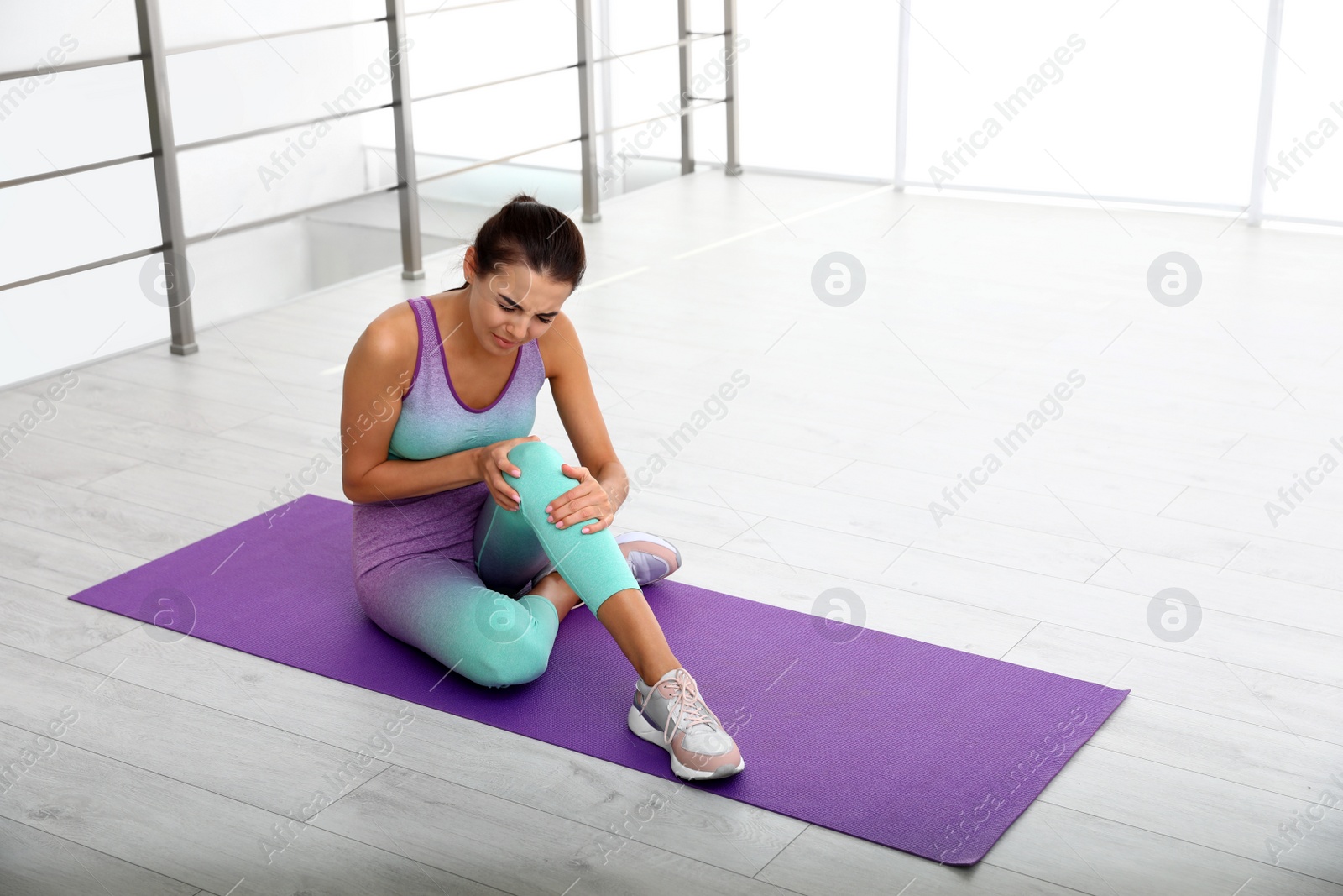 Photo of Young woman in sportswear having knee problems at gym. Space for text