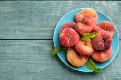 Photo of Fresh ripe donut peaches on light blue wooden table, top view. Space for text