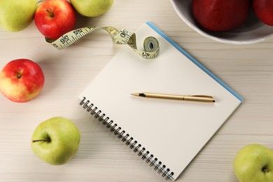 Photo of Healthy diet. Fresh apples, measuring tape, notebook and pen on light wooden table, flat lay