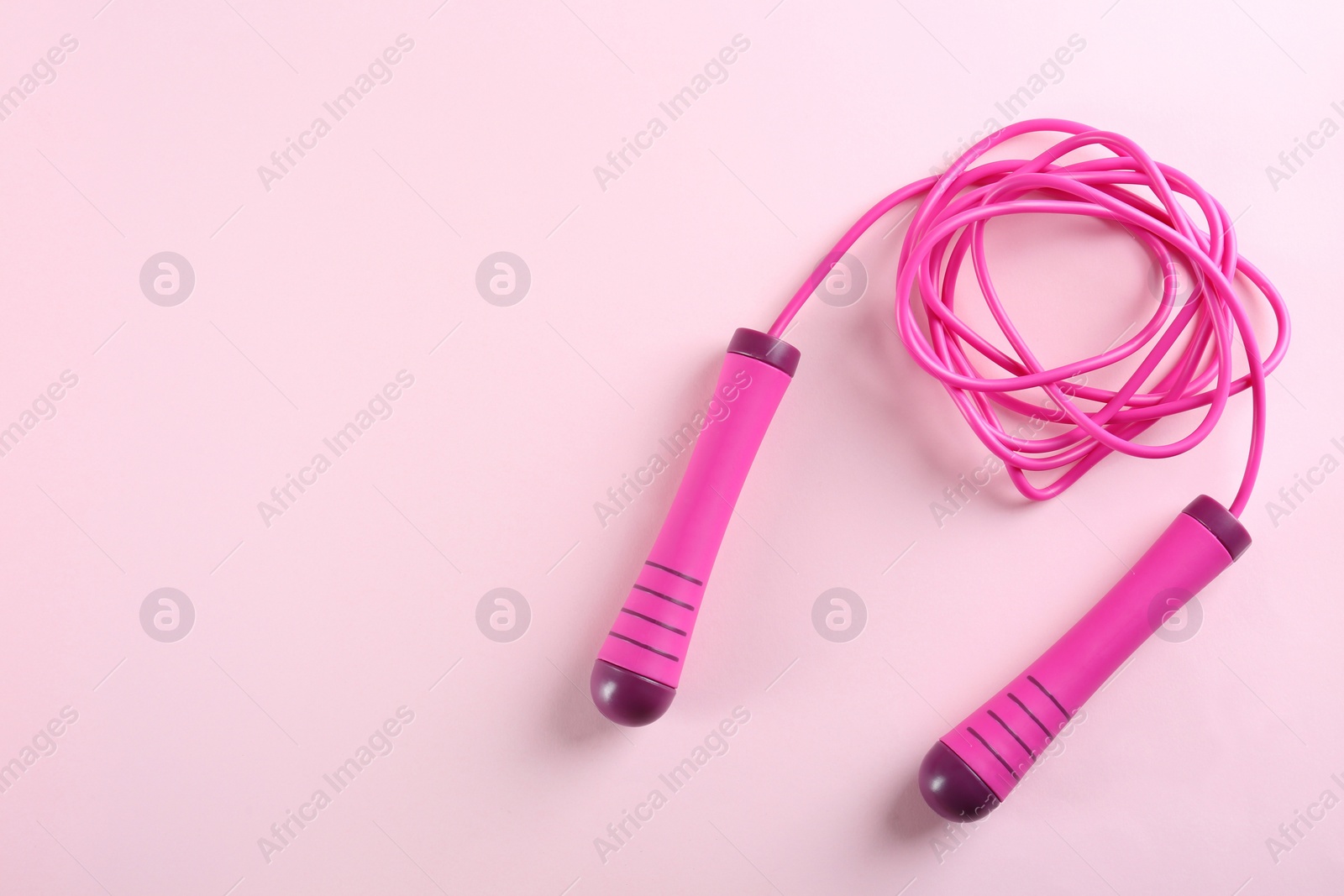 Photo of Skipping rope on pink background, top view. Space for text