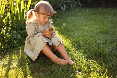 Photo of Cute little girl with chick on green grass outdoors, space for text. Baby animal