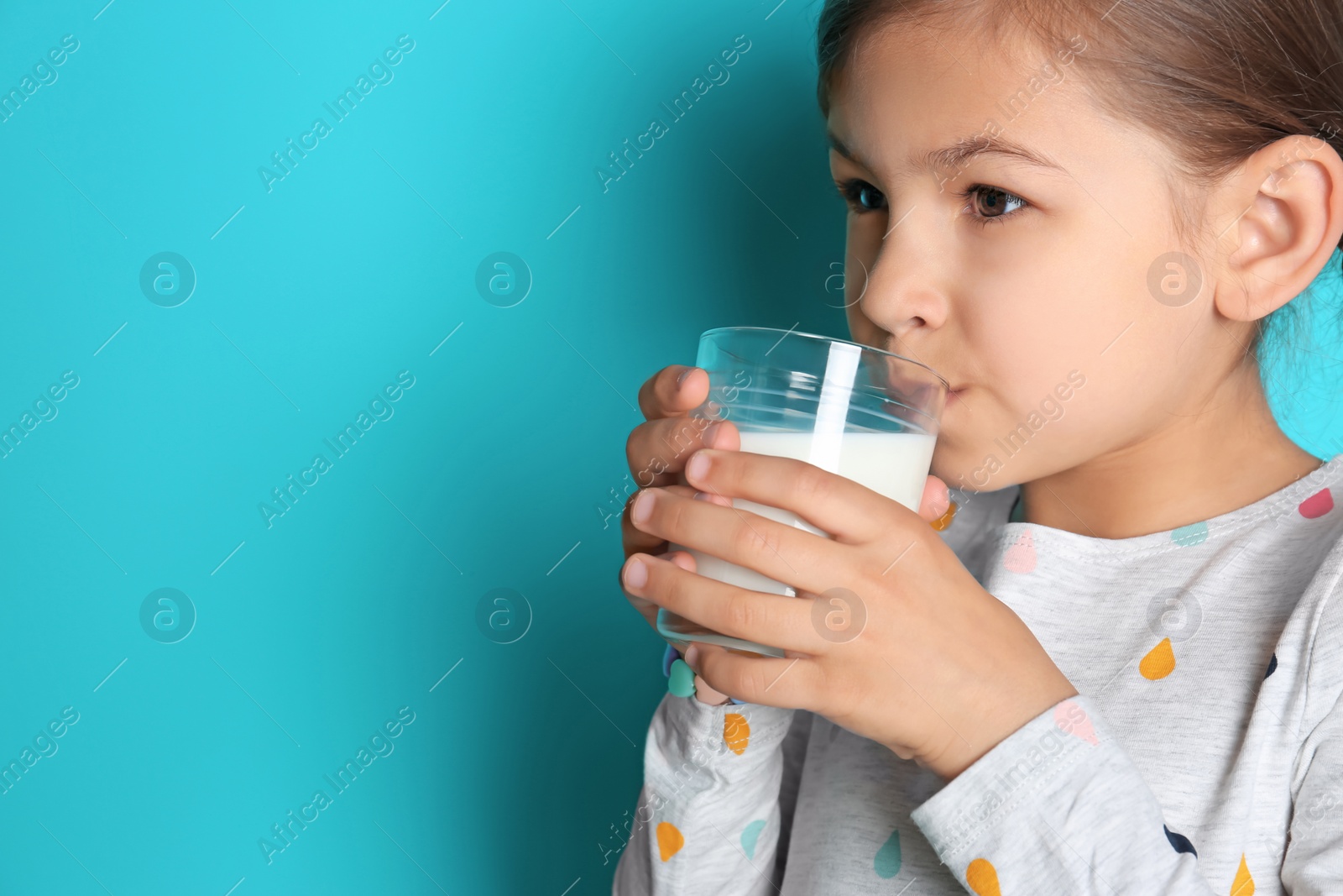 Photo of Cute little girl drinking milk on color background