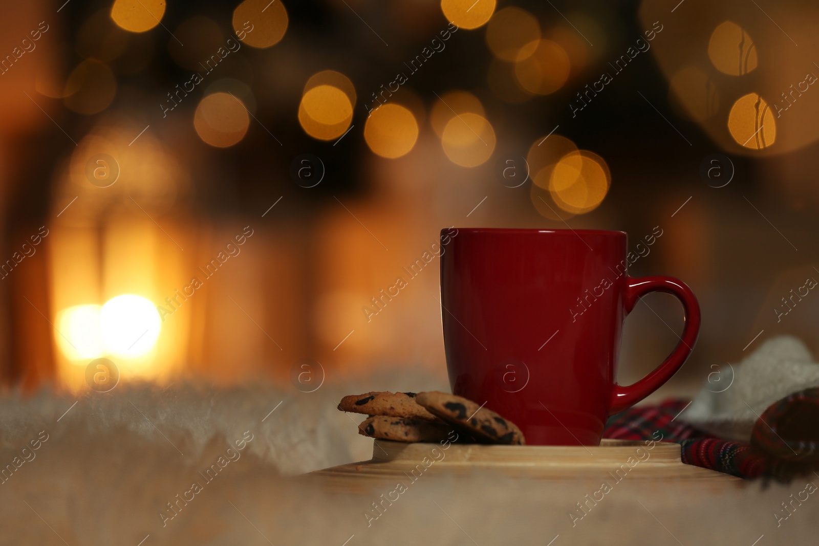 Photo of Cup of drink on white fur against blurred lights, space for text. Cozy winter