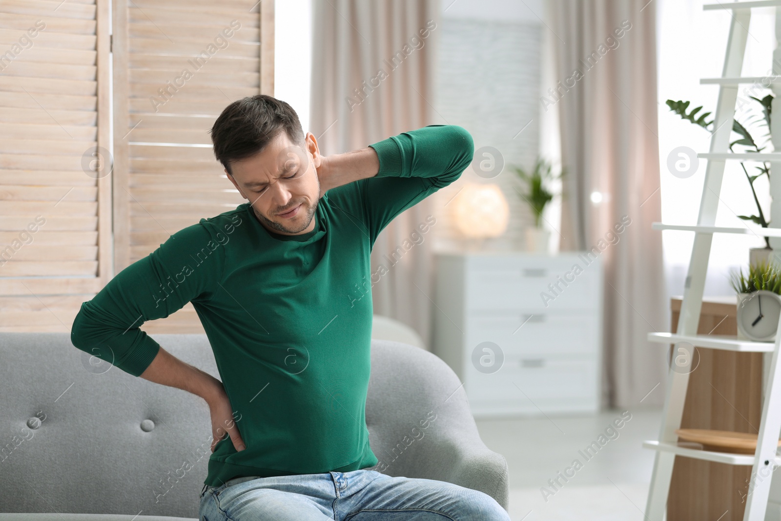 Photo of Young man suffering from back pain at home