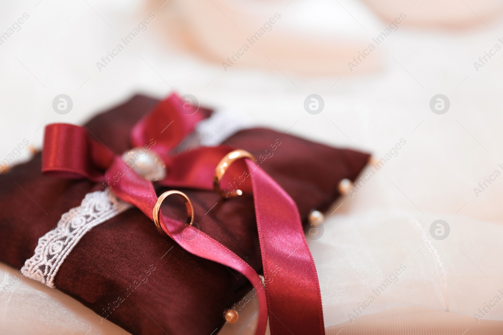 Photo of Decorative pillow with wedding rings on light background, closeup