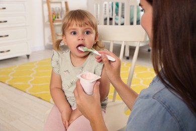 Mother feeding her cute little child with yogurt at home