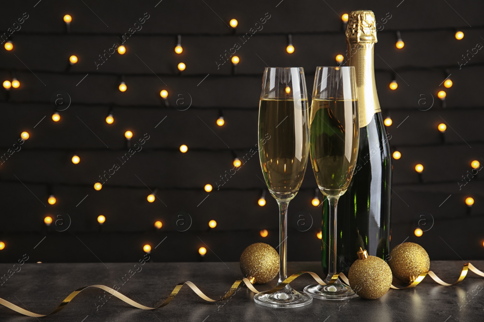 Photo of Glasses of champagne with bottle and festive decor on table against blurred fairy lights