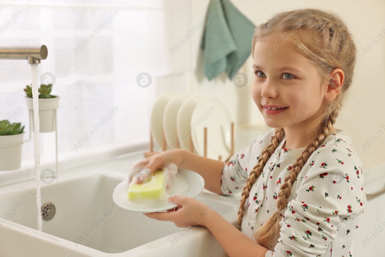 Photo of Happy girl washing plate above sink in kitchen