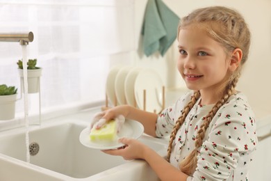 Happy girl washing plate above sink in kitchen