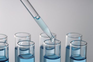 Photo of Dripping light blue liquid from pipette into test tube on gray background, closeup