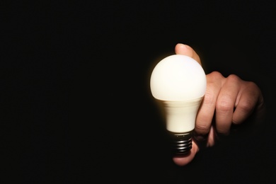 Man holding modern lamp bulb on dark background, closeup. Space for text