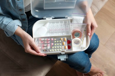 Woman holding first aid kit indoors, top view