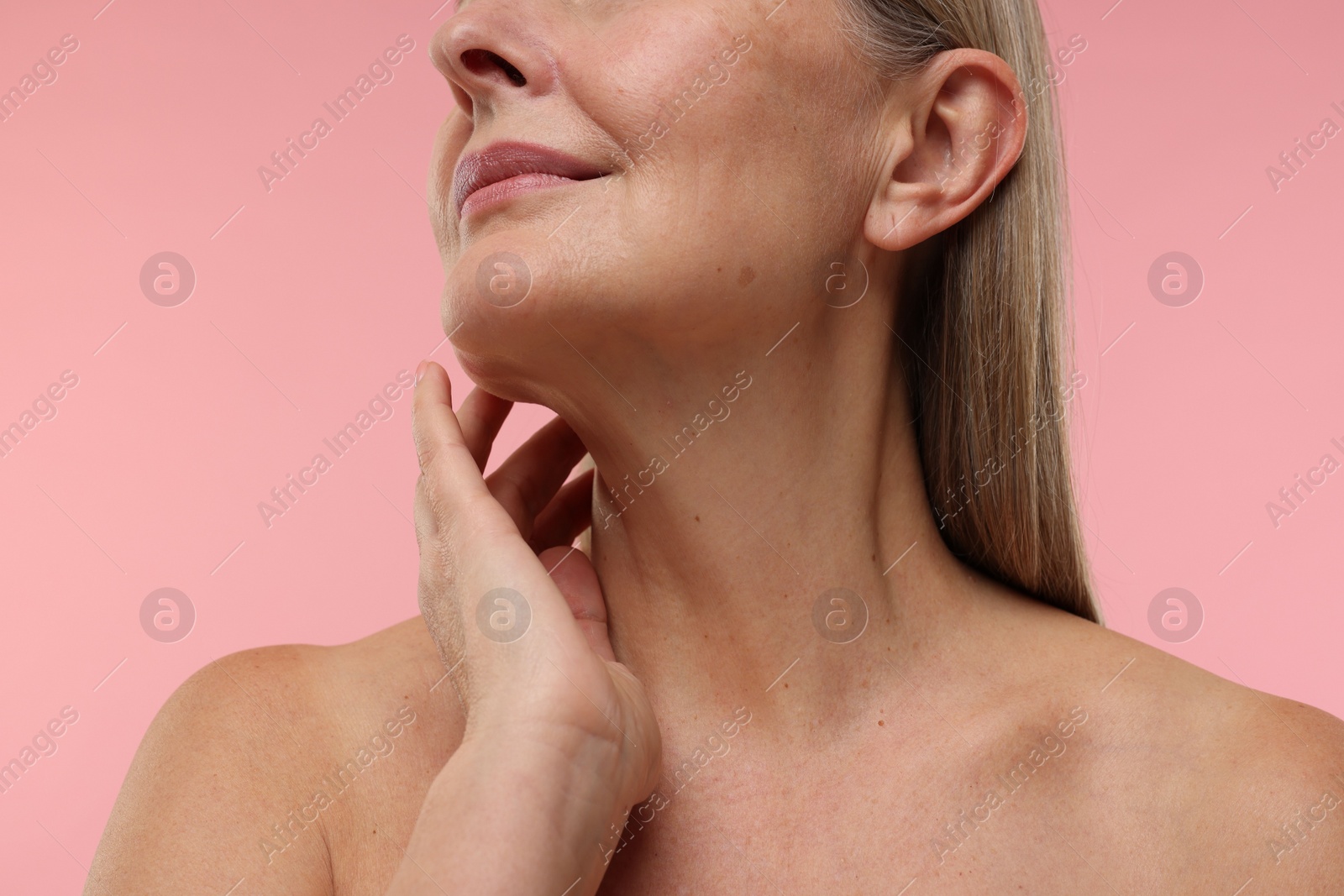 Photo of Mature woman touching her neck on pink background, closeup