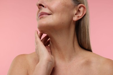 Photo of Mature woman touching her neck on pink background, closeup