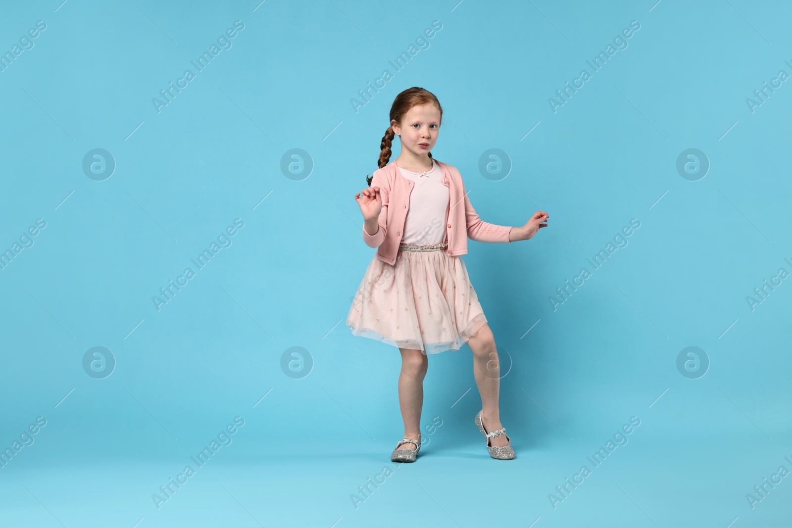 Photo of Cute little girl dancing on light blue background