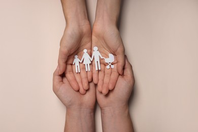 Photo of Couple holding paper family figures on beige background, top view. Insurance concept