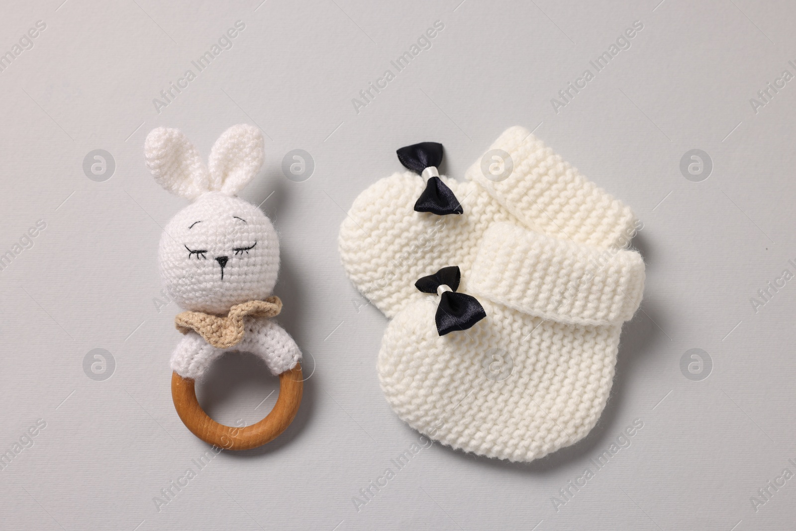 Photo of Baby accessories. Rattle and knitted booties on grey background, top view