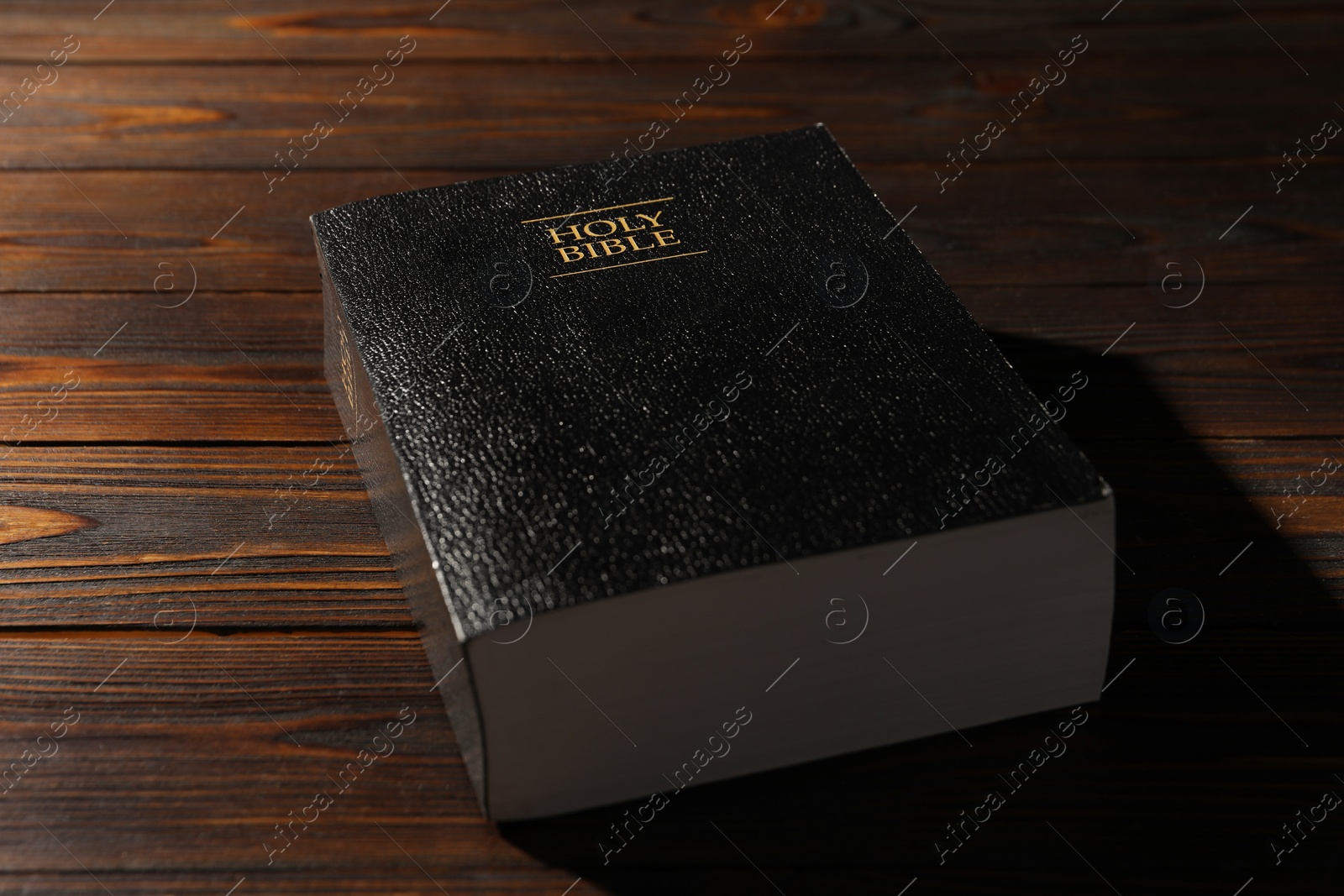 Photo of Bible with black cover on wooden table, closeup. Christian religious book