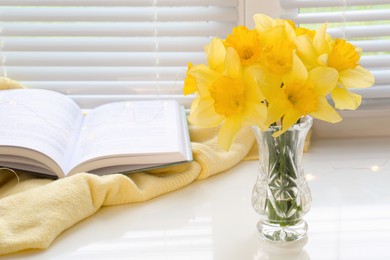 Photo of Beautiful yellow daffodils in vase and book on windowsill. Space for text