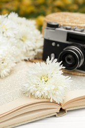 Photo of Composition with beautiful chrysanthemum flowers, vintage camera and book on white table outdoors, closeup