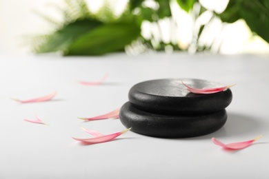 Photo of Stacked spa stones with flower petals on table. Space for text