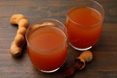 Photo of Tamarind juice and fresh fruits on wooden table, closeup