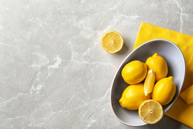 Bowl with ripe lemons on light background, top view