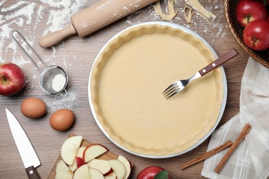 Photo of Flat lay composition with raw dough, fork and ingredients on wooden table. Baking apple pie