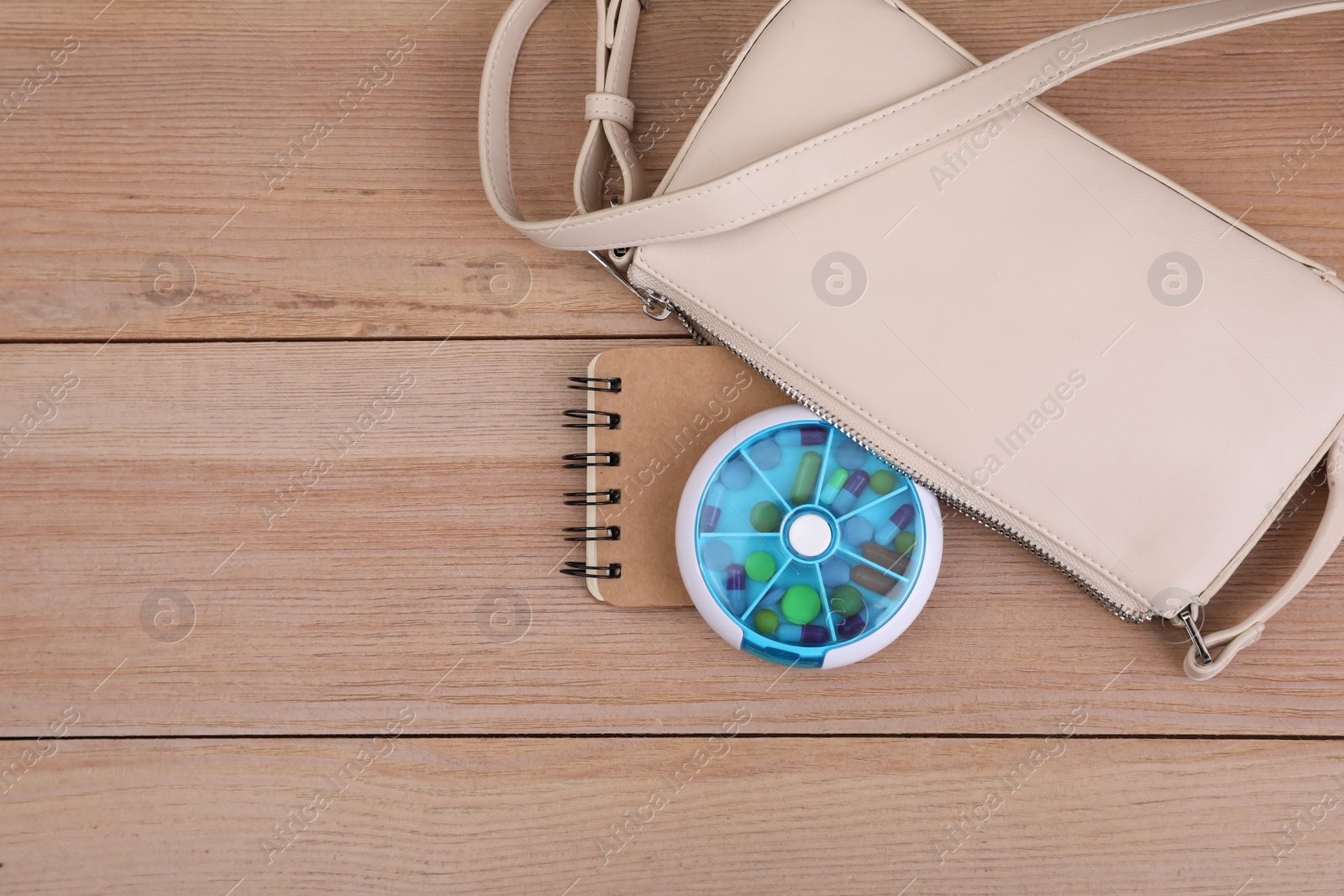 Photo of Stylish women's bag with plastic pill box and notebook on wooden background, flat lay. Space for text