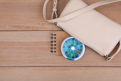 Stylish women's bag with plastic pill box and notebook on wooden background, flat lay. Space for text