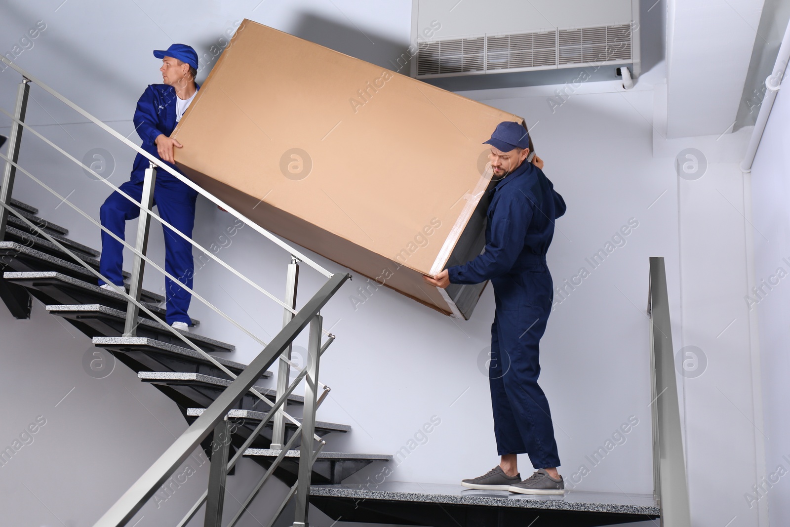 Photo of Professional workers carrying refrigerator on stairs indoors