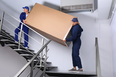 Professional workers carrying refrigerator on stairs indoors