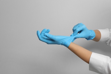 Doctor putting on medical gloves against light grey background, closeup. Space for text