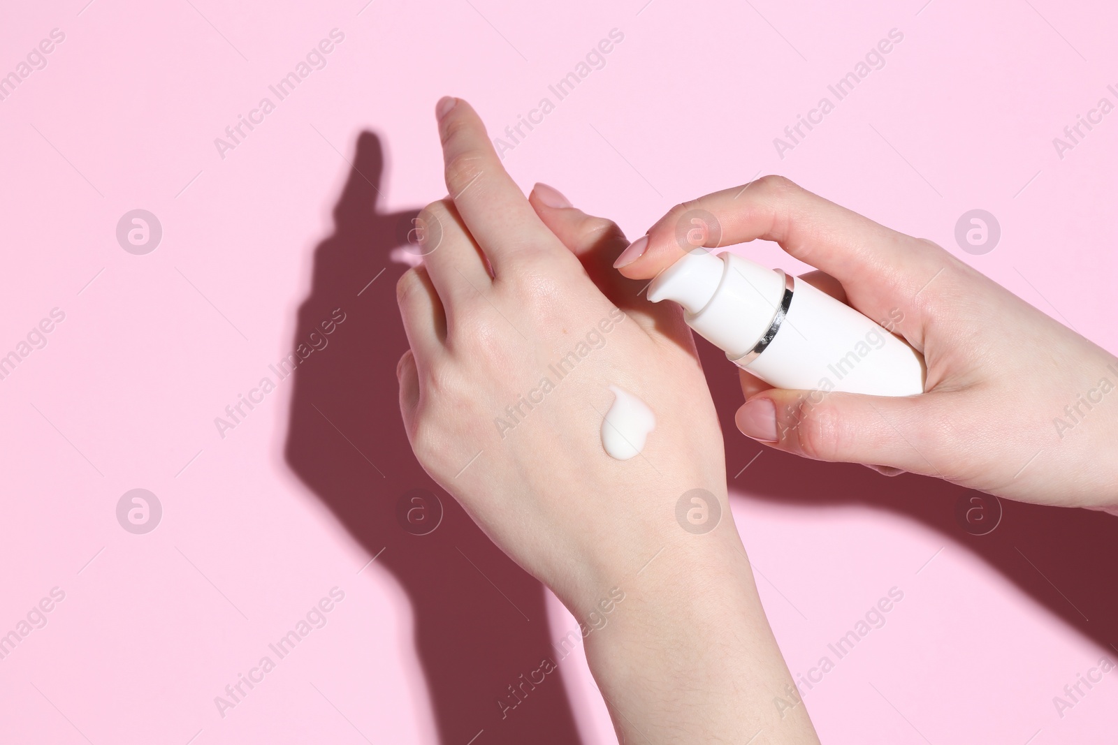 Photo of Woman applying cream on her hand against pink background, closeup