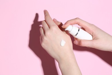 Woman applying cream on her hand against pink background, closeup