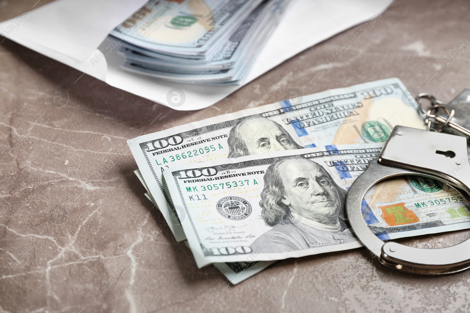 Photo of Dollar bills and handcuffs on brown marble table, closeup. Bribe concept