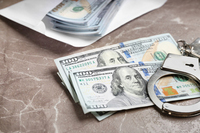 Photo of Dollar bills and handcuffs on brown marble table, closeup. Bribe concept