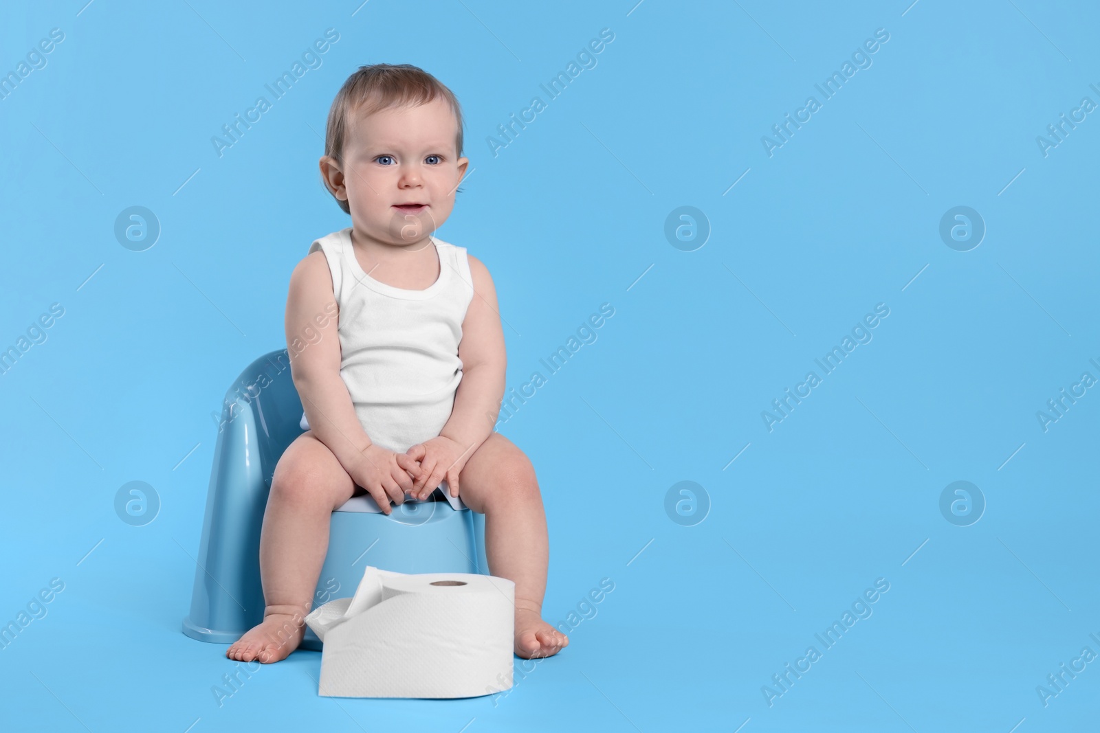 Photo of Little child sitting on baby potty and toilet paper roll against light blue background. Space for text