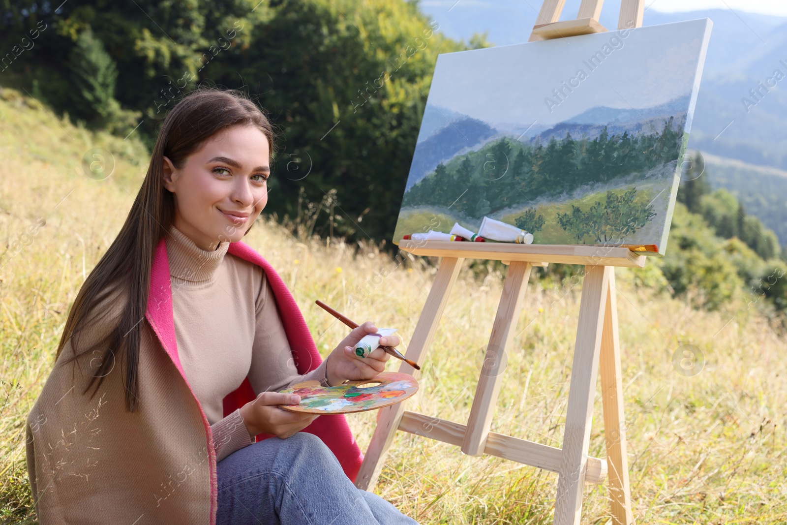 Photo of Young woman drawing on easel in mountains