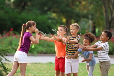 Photo of Cute little children playing with soap bubbles in park