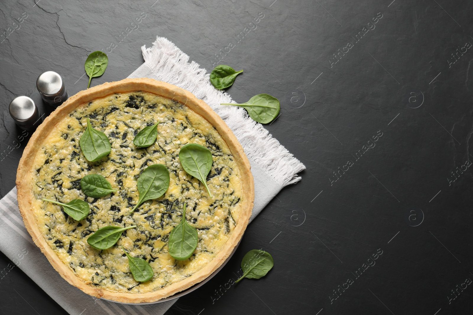 Photo of Delicious homemade spinach pie with spices on black table, flat lay. Space for text