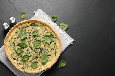 Delicious homemade spinach pie with spices on black table, flat lay. Space for text