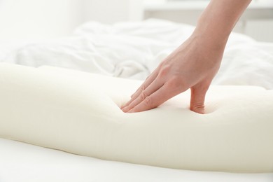 Woman touching orthopedic memory foam pillow on bed, closeup. Space for text