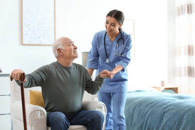 Photo of Care worker helping elderly man with stick in geriatric hospice