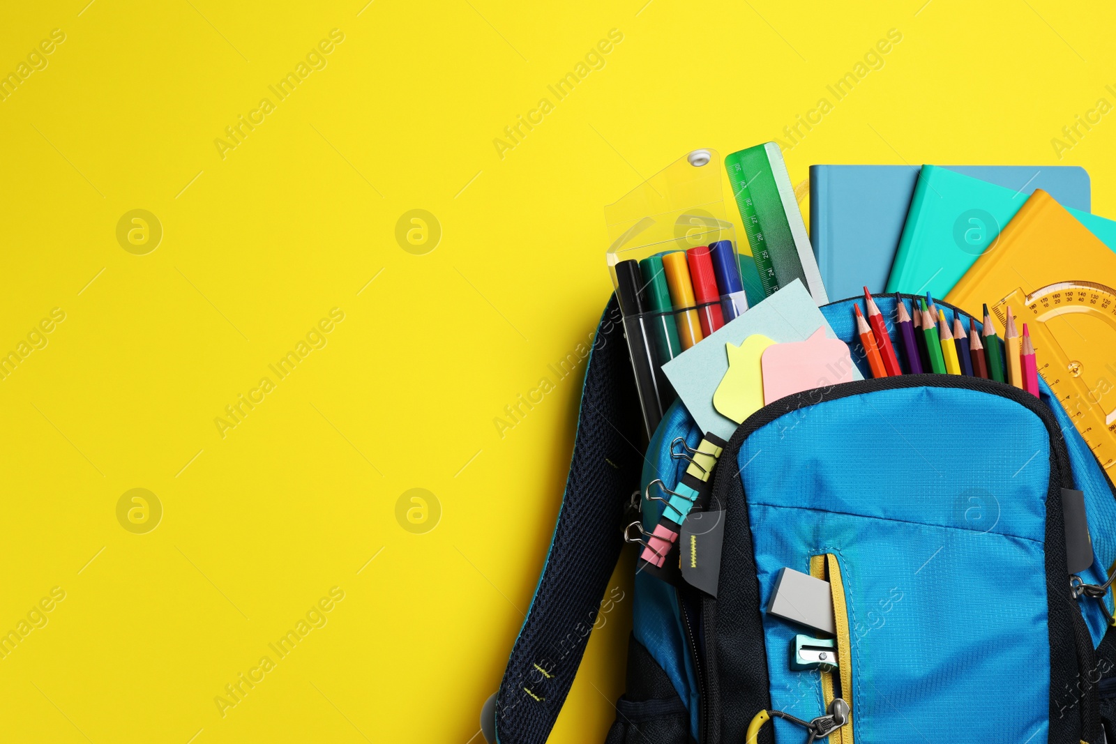 Photo of Backpack with school stationery on yellow background, top view. Space for text