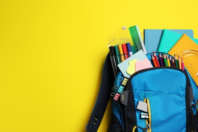 Photo of Backpack with school stationery on yellow background, top view. Space for text